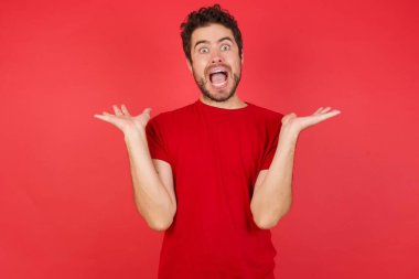 Kırmızı stüdyoda beyaz bir adam, sıradan kırmızı bir tişört giyiyor çılgın ve başarısını kutluyor kolları havada ve gözleri açık heyecanla haykırıyor. 