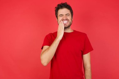 Genç beyaz bir adam diş ağrısı ya da diş hastalığından dolayı acı dolu bir ifadeyle ağzına dokunuyor.