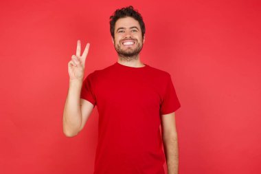 Kafkasyalı genç adam iki numarayı işaret ederken kendinden emin ve mutlu bir şekilde gülümsüyor..