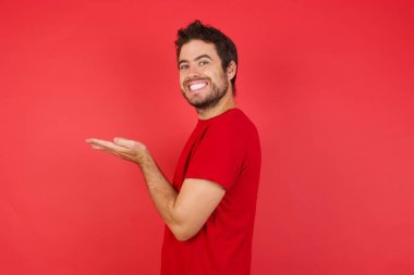 Kırmızı stüdyodaki beyaz adam avuçlarını açıp fotokopi alanını gösteriyor. Reklam sunuyor.