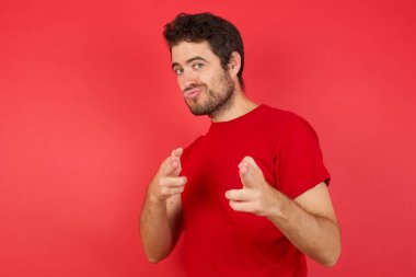 Stüdyodaki kırmızı arka planda kameraya mutlu ve küstah pozlar veren bir adam. Hey sen, bang