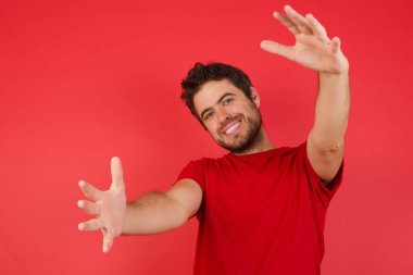 Genç yakışıklı adam kameraya bakıyor, sarılmak için kollarını açmış gülümsüyor. Mutluluğu kucaklayan neşeli bir ifade.