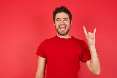 Genç yakışıklı beyaz adam izole edilmiş kırmızı arka plan üzerinde tişört giyiyor ve kameraya gülümsüyor. En sevdiği konsere gitmeye hazır..