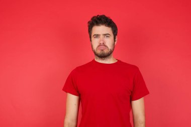 Hoşnutsuz genç beyaz adamın portresi izole edilmiş kırmızı arka planda tişört giyiyor. Surat asmalar ağlayacak gibi, mutsuz ve hoşnutsuz oldukları için hedeflerine ulaşamadıkları için, hayal kırıklığına uğramış genç adamın sorunları var.