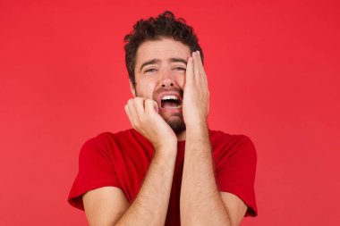 Üzgün, çaresiz, ağlayan, kırmızı arka plan üzerine tişört giyen beyaz bir adam karısı ya da kız arkadaşıyla tartıştıktan sonra depresyona girmiş, stresli görünüyor, suratını asıyor. Yakışıklı erkek kendini yalnız ve endişeli hissediyor.