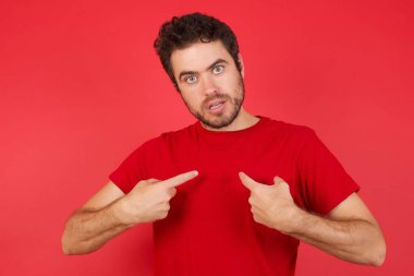 Utanmış genç, beyaz bir adamın kırmızı arka plan üzerinde tişört giymesinin fotoğrafı şaşkın bir ifadeyle yarışmaya katılmak için seçildiğini, bir konuda tereddüt ettiğini gösteriyor. 