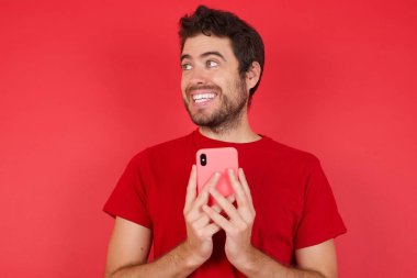 Copyspace Genç yakışıklı beyaz adam izole edilmiş kırmızı arka plan üzerinde tişört giyiyor sosyal medyada bir şeyler oluyor 