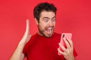 Yakından çekilmiş bir portre. Tişört giyen yakışıklı beyaz bir adam. İzole edilmiş kırmızı arka plan. 