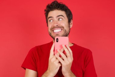 İzole edilmiş kırmızı arka plan üzerinde tişört giyen yakışıklı beyaz bir adamın portresi. Yeni hücreyi gösteriyor.