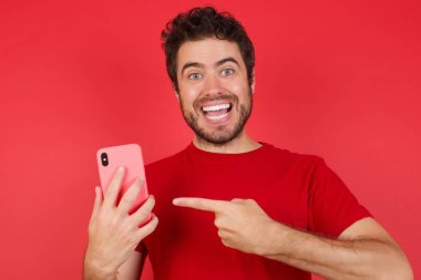 İzole edilmiş kırmızı arka plan üzerinde tişört giyen yakışıklı beyaz bir adamın portresi. Yeni hücreyi gösteriyor.,