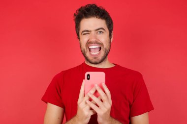 İzole edilmiş kırmızı arka planda tişört giyen yakışıklı beyaz adam başarıyı kutlayan bir selfie çekiyor.