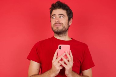 İzole edilmiş kırmızı arka planda tişört giyen yakışıklı beyaz bir adam. El ele tutuşmuş, iyi gençlik haberleri okuyor. Boş yer ilanı gibi. 
