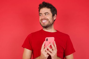 İzole edilmiş kırmızı arka plan üzerinde tişört giyen yakışıklı beyaz bir adam. El ele tutuşun. İyi gençlik haberleri okuyun. Boş yer reklamı yapın. 