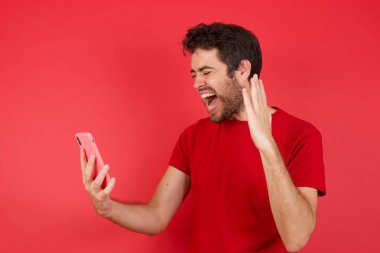 Kızgın, genç, beyaz bir adam izole edilmiş kırmızı arka plan tişörtü giyip telefonda bağırıyor ve bir çalışanla tartışıyor. İşte sorunlar var..