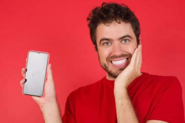 İzole edilmiş kırmızı arka plan üzerine tişört giyen yakışıklı beyaz adam el ele tutuşun modern teknoloji dokunun.