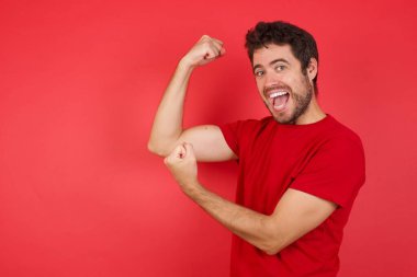 Heyecanlı genç beyaz bir adamın kırmızı arka plan üzerinde tişört giyip Kara Cuma alışverişini kutlayan yumruklarını kaldırırken profil fotoğrafı. 