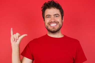 İzole edilmiş kırmızı arka plan üzerinde beyaz tişört giyen genç yakışıklı adam işaret dili Çince olan parmaklarıyla 6 numara Liu 'yu gösteriyor.