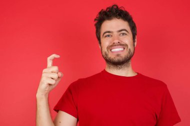 İzole edilmiş kırmızı arka plan üzerine tişört giyen yakışıklı beyaz adam Çince işaret dili Jiu 'nun dokuz numaralı parmaklarını işaret ediyor.