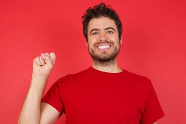 İzole edilmiş kırmızı arka plan üzerinde tişört giyen yakışıklı beyaz adam Çince işaret dilinde on numara Shi 'yi işaret ediyor.