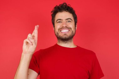 İzole edilmiş kırmızı arka plan üzerinde tişört giyen yakışıklı beyaz adam Çince işaret dilinde on numara Shi 'yi işaret ediyor.