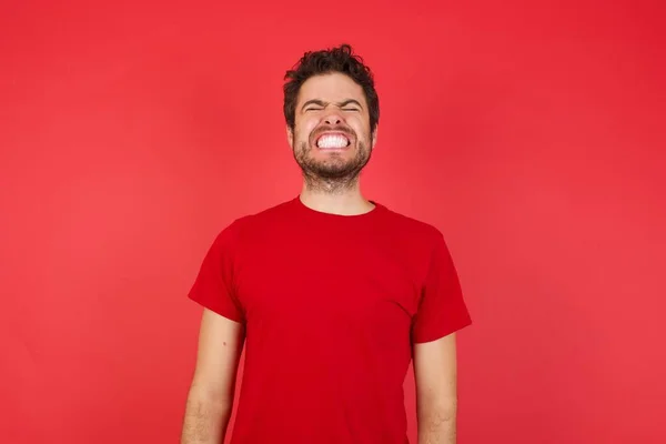 Mladý Pohledný Běloch Ukazuje Zuby Zavřenýma Očima Červeném Pozadí — Stock fotografie
