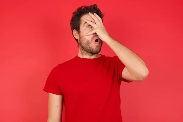 Jovem Caucasiano Bonito Vestindo Camiseta Sobre Fundo Vermelho Isolado Espreitando — Fotografia de Stock