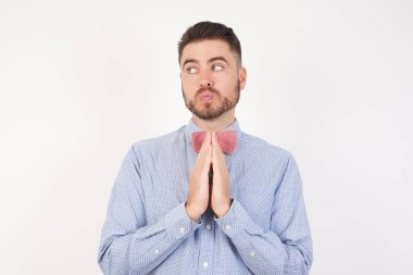 Resmi gömlek ve papyon giymiş Avrupalı bir adam beyaz stüdyo arka planına karşı poz veriyor. El ele tutuşup bir fikir oluşturuyorlar. Bak askance. 