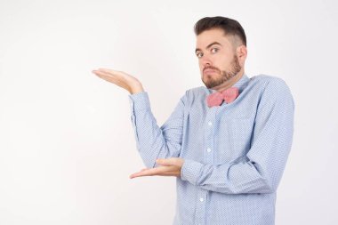 Yakışıklı iş adamı, gri arka planda duruyor. İki eliyle işaret ediyor. 