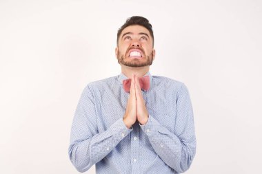 Beyaz arka planda izole edilmiş genç beyaz adam umutla el ele yalvarıyor ve dua ediyor.