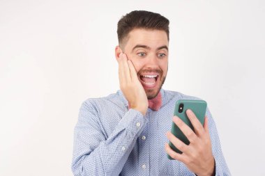 Stüdyoda gömlek ve papyon takan ve elinde akıllı telefon olan mutlu bir adam. 