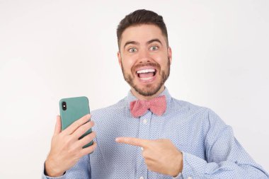 Stüdyoda gömlek ve papyon takan ve elinde akıllı telefon olan mutlu bir adam. 