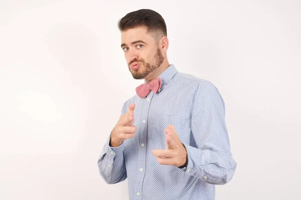 셔츠와 나비넥타이를 쾌활하고 카리스마있는 남자가 스튜디오 배경에서 윙크를 손가락으로 권총을 — 스톡 사진