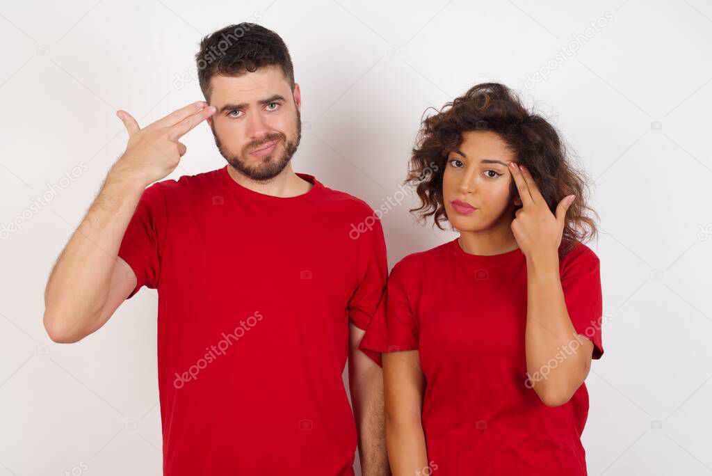 Unhappy brunette hair man and woman in studio, make suicide gestures and imitates guns with hands, curves lips keeps two fingers on temple, shoots, problem fingers on temple