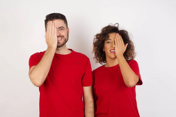 man and woman in studio, covering eyes with hands and smiling on camera