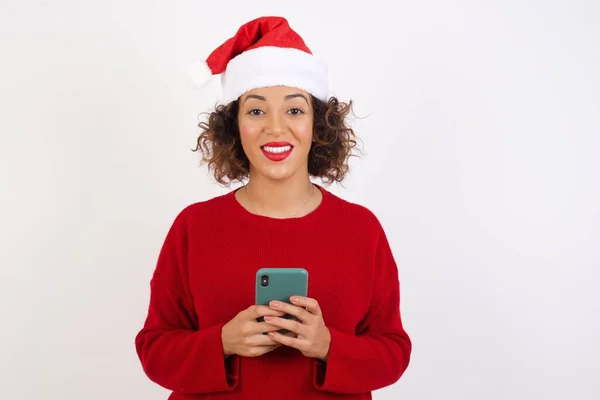 Noel Baba Şapkalı Kadın Stüdyoda Cep Telefonunu Karıştırıyor Gülümsüyor Kameraya — Stok fotoğraf