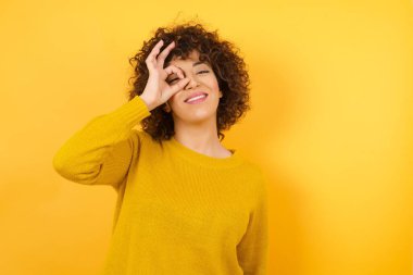 Sarı stüdyodaki gülümseyen kadın, tamam tabelasından bakıyor. 