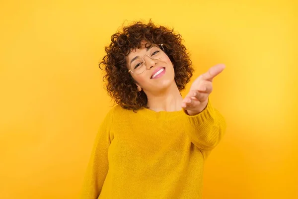 Glimlachende Vrouw Met Krullend Haar Gele Studio Lachend Vriendelijk Aanbieden — Stockfoto