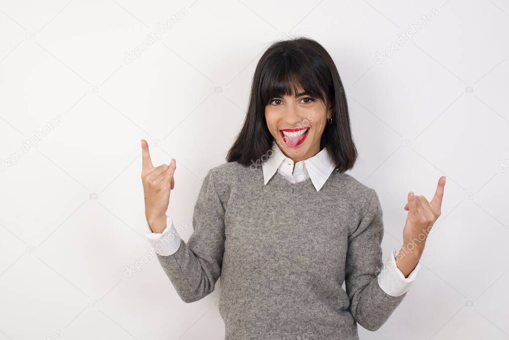 Young brunette woman posing in studio. making rock hand gesture and showing tongue