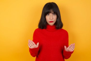 Ciddi bir kadın günlük giysiler giyer, sarı duvarda izole bir şekilde avuçlarını kameraya çeker, jestleri durdurur, duygularını kontrol etmesini ve gergin olmamasını ister.