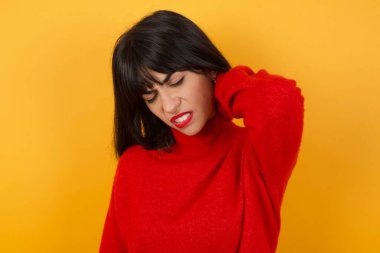 İzole edilmiş sarı arka planda duran genç beyaz kadın. Boyun ağrısı, elinle boynuna dokunmak, kas ağrısı.