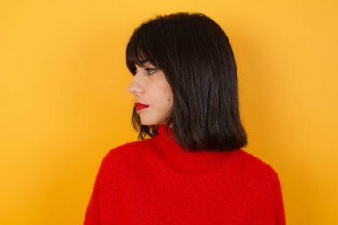 Sarı arka planda dikilen beyaz kadının yan profil fotoğrafını kapat.  