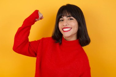 Beyaz kadın sarı arka planda kaslarını gösteriyor.