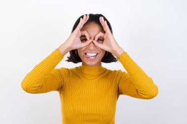 Güzel, genç bir kadın dürbün gibi jest yapıyor. Dilini dışarı çıkarıyor, gözleri parmaklarından bakıyor. Çılgın ifade.