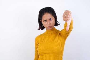 Güzel genç bir kadın kızgın, sinirli, hayal kırıklığına uğramış ya da hayal kırıklığına uğramış hissediyor. Beyaz duvara karşı ciddi bir bakış atıyor.