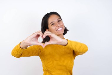 Gülümseyen ve elleriyle kalp sembolü yapan bir model. Romantik konsept.