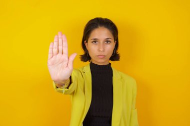  Güzel genç bir kadın avuç içiyle jesti durduruyor. Yüzünde olumsuz ve ciddi bir jest olan uyarı ifadesi 