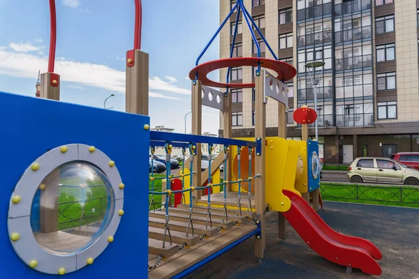 Children playground on yard activities in public park surrounded by green trees at sunlight morning. Children run, slide, swing,seesaw on modern playground. Urban neighborhood childhood concept. — Stock Photo, Image