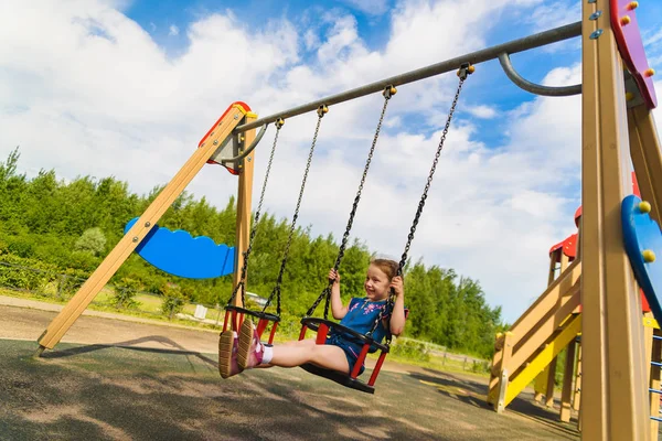 Dzieci bawią się na odkrytym placu zabaw w deszczu. Dzieci bawią się w szkole lub na podwórku przedszkola. Aktywny dzieciak na kolorowej huśtawce. Zdrowe letnie aktywności dla dzieci w deszczowej pogodzie. Mały chłopiec swinging. — Zdjęcie stockowe