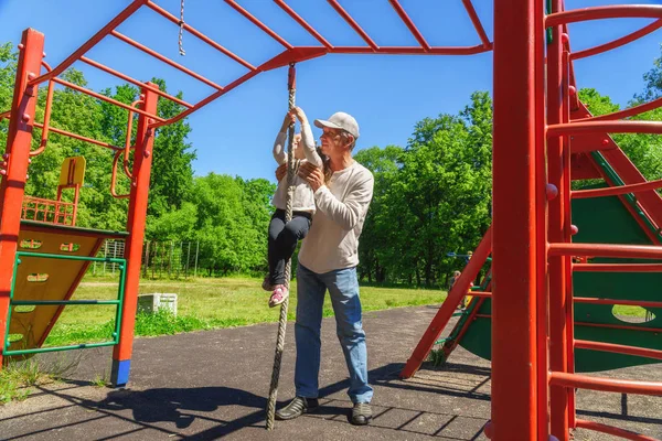 父は子供の娘がロープを登るのを手伝う。若者を助けるという概念 — ストック写真