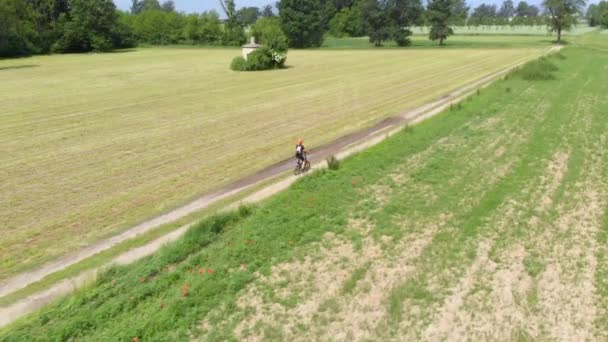空中慢动作 人骑自行车沿着乡间小路经过耕地和农田 生态友好交通循环车道 — 图库视频影像